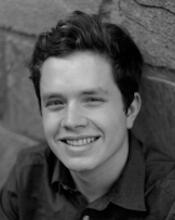 Black & white photo of Will's smiling face in a collared shirt in front of a brick background