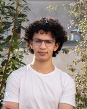 Samuel Ostrove looking at camera with plants and buildings in the background.